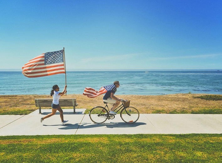 A couple riding their bikes by the sea waving the U.S. flag on the 4th of July.